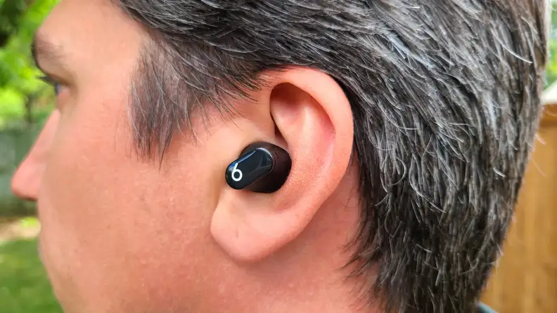 A man with brown and grey hair is shown from the back with the black Beats Studio Bud in his left ear.