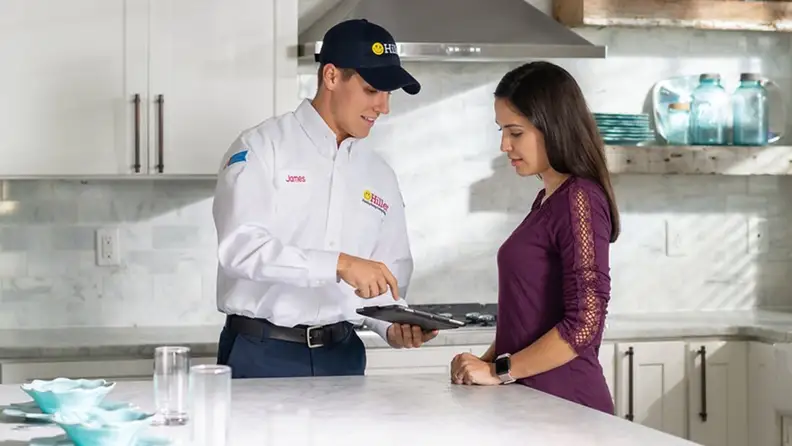 Technician showing a tablet to a customer in her kitchen