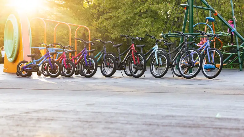 A row of kids' bikes lined up by size from smallest to largest at a sunny playground.