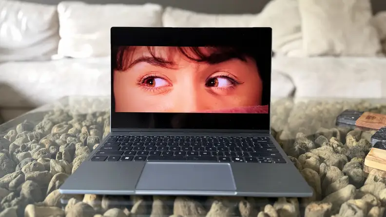 Dell XPS 13 on glass table showing top half of woman's face on the display screen.