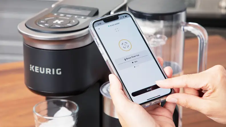 A close up of a person using the app on a smartphone to control the Keurig K-Cafe Smart coffee machine.