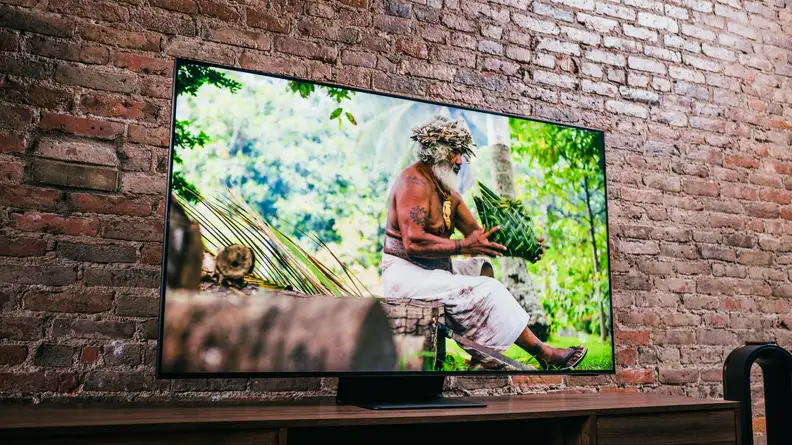 A muscular elder man sitting in a sunlit rainforest on the TV's screen
