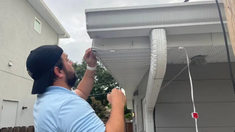 A man hanging up the Govee Permanent Outdoor lights on a house exterior.