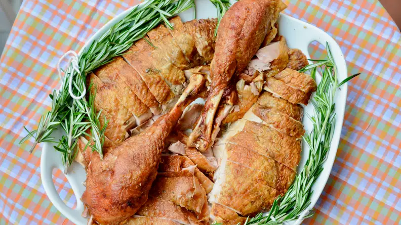 A photo of a carved turkey cut into pieces on a serving platter, with rosemary garnish.