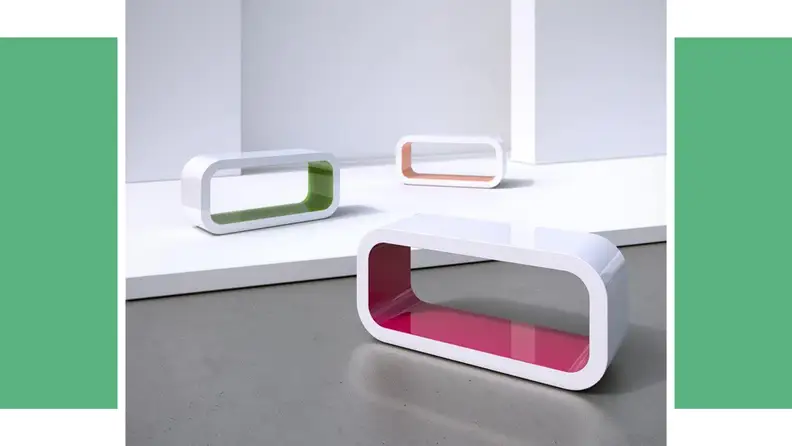 A uniquely-shaped coffee table in front of a green background.
