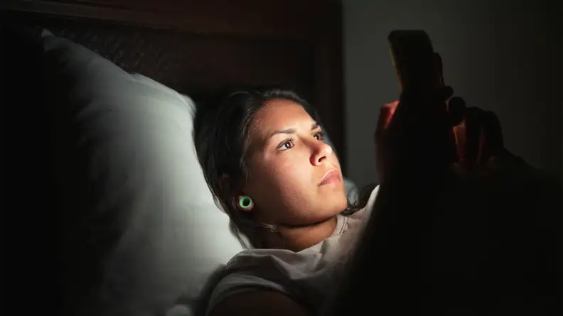 A photo of a woman using her phone at night.