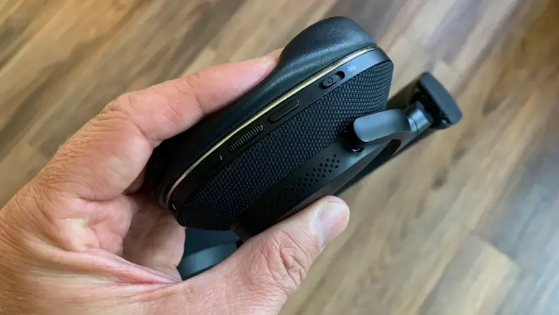 A hand squeezes the ear cup pad of the Px7 S2 above a wooden floor.