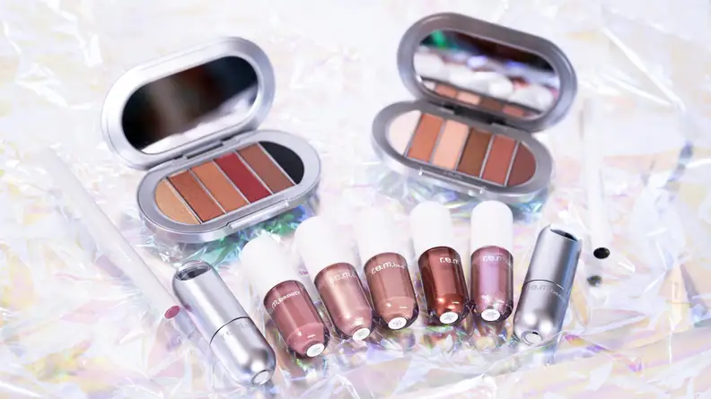Two eyeshadow palettes, five liquid eyeshadows, an eyeliner, and a lip stain all laying on holographic cellophane.