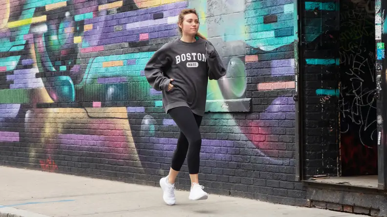 Person running outdoors next to a painted brick wall while wearing a pair of white lululemon Beyondfeel sneakers.