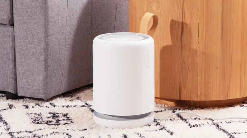 A portable air purifier sits on a patterned carpet next to a couch and a side table.