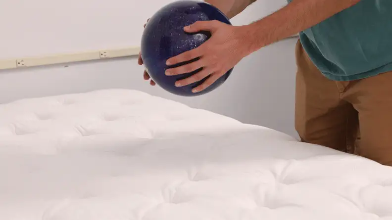 Person dropping a bowling ball onto the WinkBed hybrid mattress to test durability.