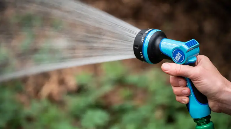 A person sprays water out of a blue Aqua Joe hose nozzle.