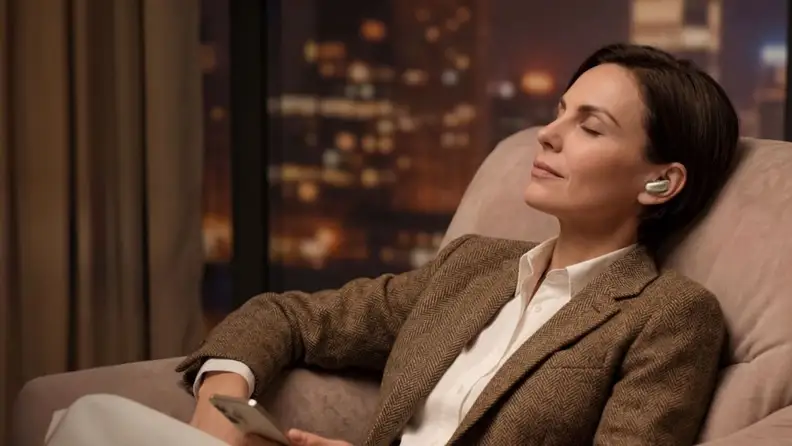 Woman sitting back in a chair listening to Soundcore Liberty 5 Pro Max earbuds while holding a phone.
