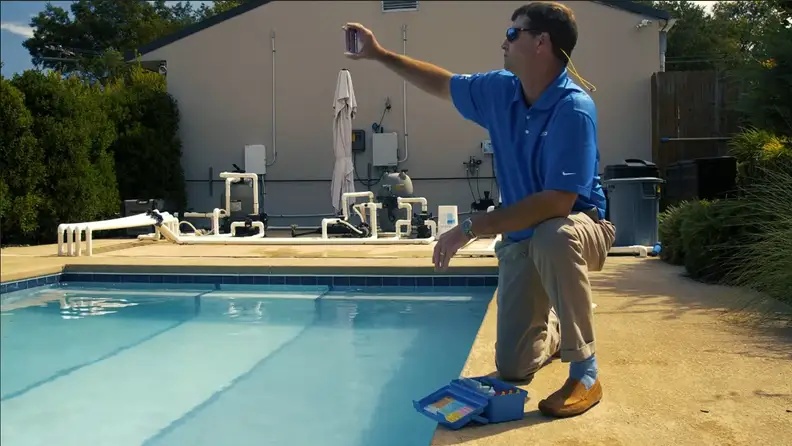 Man kneeling poolside testing water with a chemical test kit