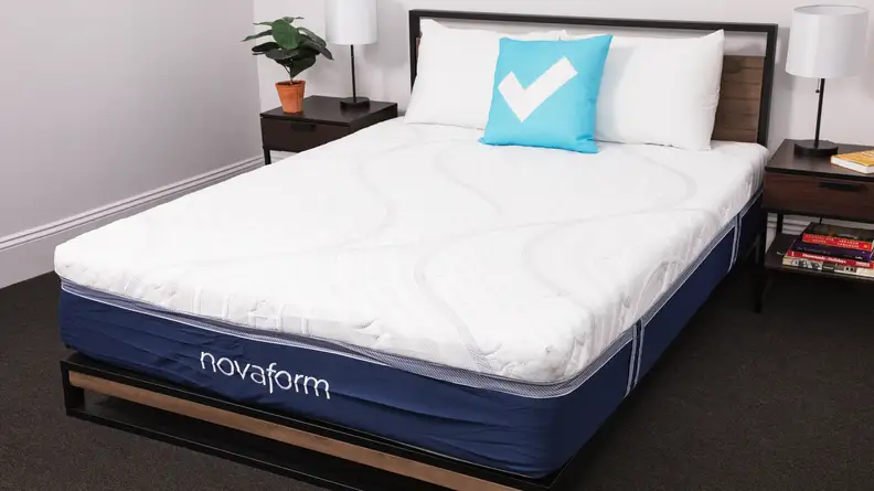A made-up bed with white pillows and a blue checkmark pillow in a bedroom.