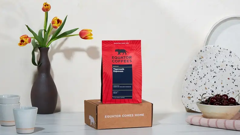 Coffee bag on a box beside tulips and a bowl of cherries