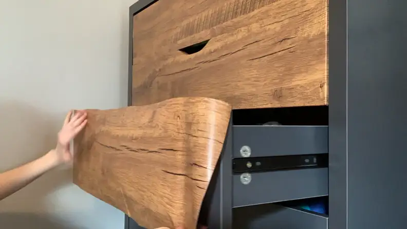 Pressing peel and stick wood-textured contact paper onto gray dresser