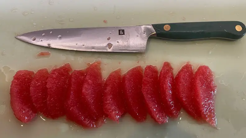 Hedley & Bennett knife sitting next to row of red citrus fruit on top of cutting board.