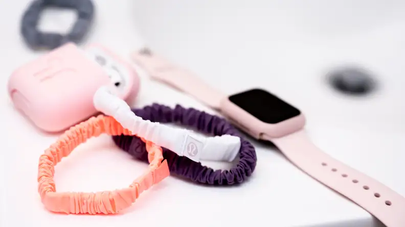 Three colorful Lululemon hair scrunches sitting next to a set of Airpods and an Apple Watch on a white vanity.