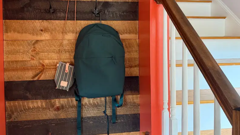 A green back pack hanging on a wood wall