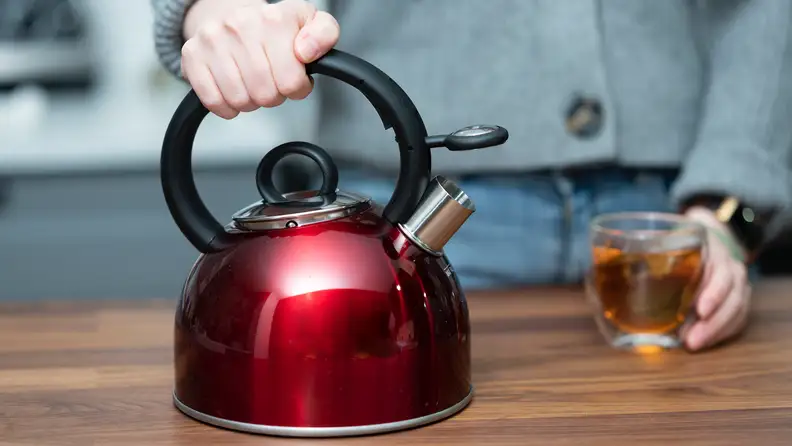 A red Cuisinart Aura teapot sits on a kitchen counter.
