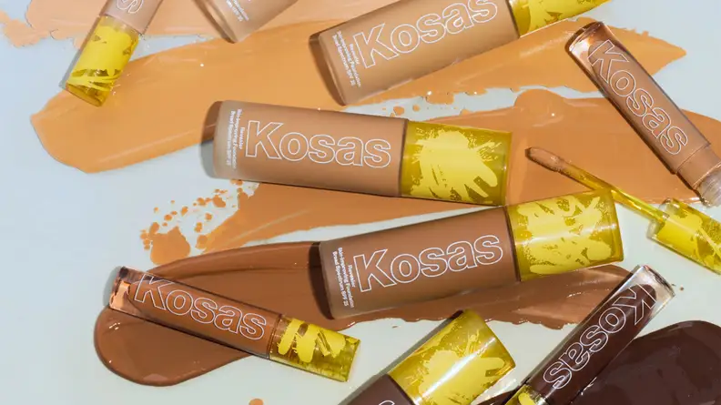 Bottles of concealer and foundation lay among each other on a background of foundation swatches in different skin tone shades.