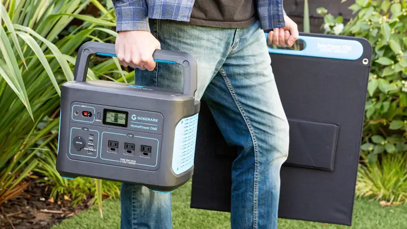Person holding portable generator and solar panel outdoors.