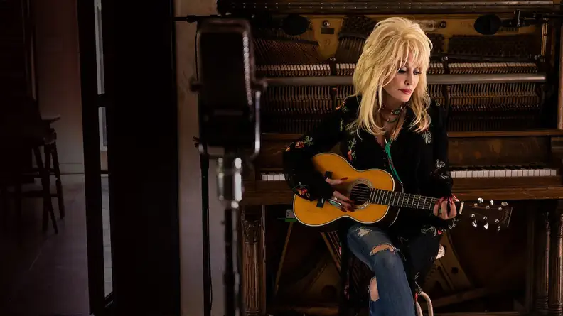 Dolly Parton with a guitar, as seen in "Dolly Parton: Here I Am," one of the best celebrity documentaries to stream now.
