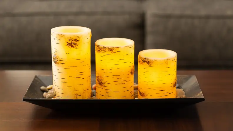 A trio of yellow Birch Bark Candlescape candles glow on a living-room table. They have no flame.