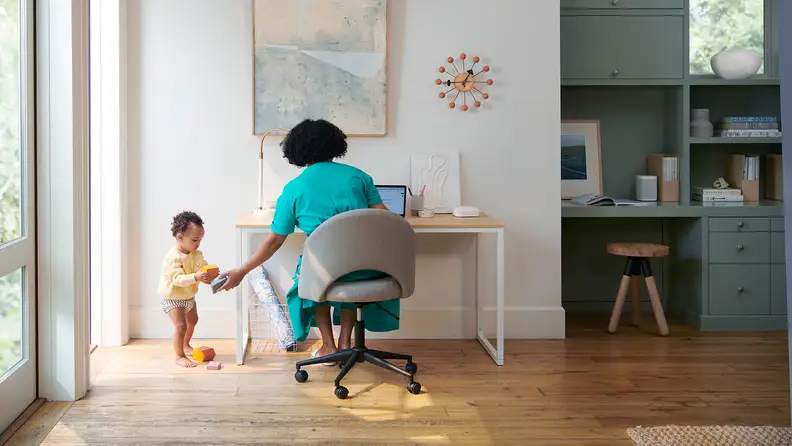 A woman hands a baby a toy as she works on her laptop