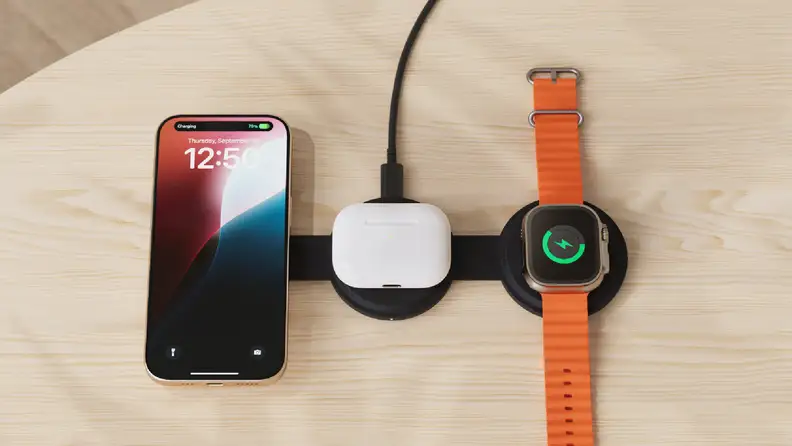 A sleek wireless charging station on a wooden surface, simultaneously powering an iPhone, a pair of AirPods, and an Apple Watch with an orange band.
