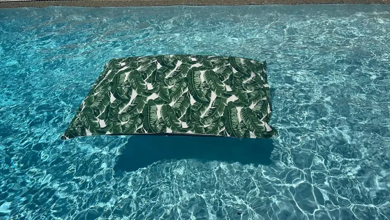 Empty Laze Pillow pool float in a fiddle leaf print floating in blue pool water.