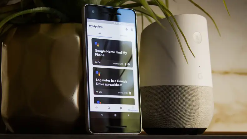 A phone running IFTTT next to a Google Home speaker