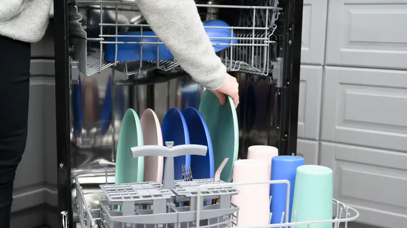 The GE GPT225SSLSS portable dishwasher, open and being filled with colorful pastel dishes.