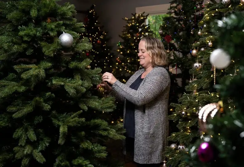 Person hanging up ornaments on an artificial tree next to many other artificial trees