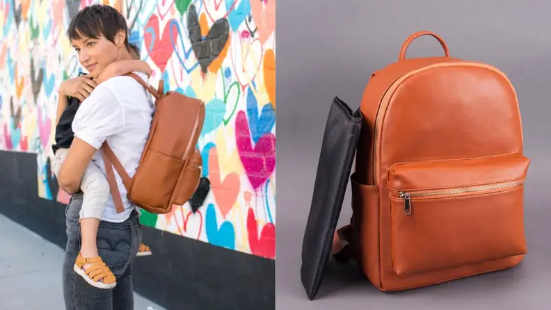 A mom holds a child while she wears the backpack and diaper bag. A still of the diaper bag.