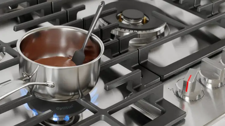 Small stainless steel pot cooking melted chocolate on stovetop.