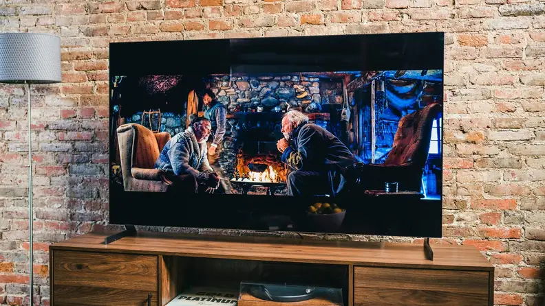 Flat screen smart TV playing movie in front of brick wall indoors.