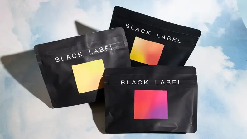 Three black Black Label pouches with colorful gradient squares against a cloudy backdrop