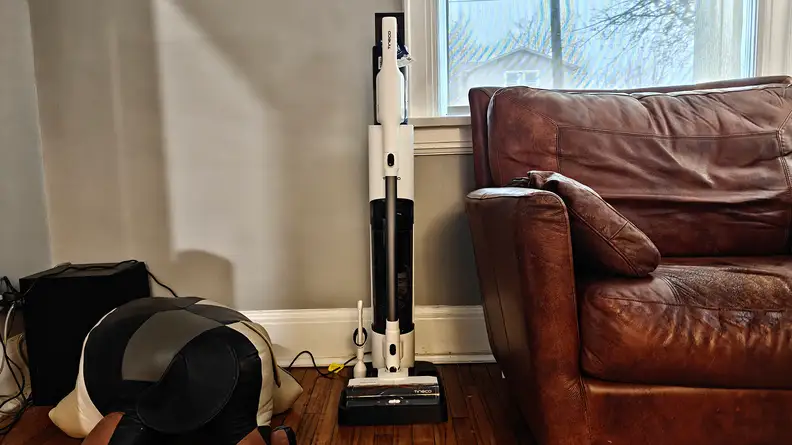 The Tineco Pure One Station 5 stands in a living room next to a big leather arm chair