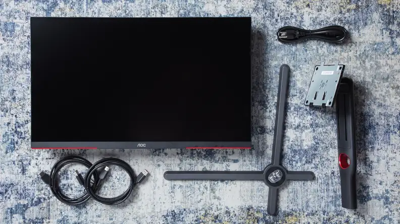 The AOC Q27GX3MN gaming monitor on a rug features accessories.