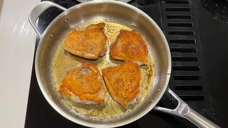 Four piece of meat being cooked in a stainless steel pan on a black stovetop.