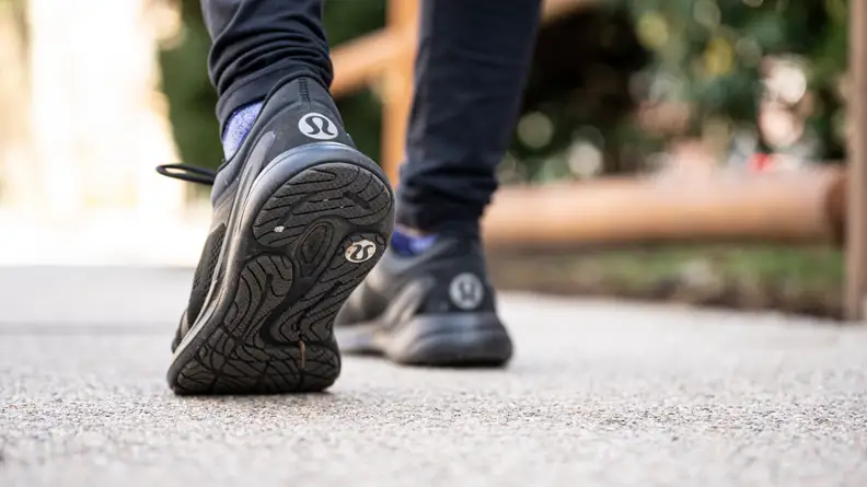 Feet wearing black Lululemon shoes with the brand's logo in white on the heel