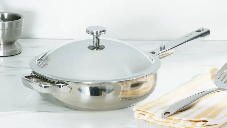 Titanium Always Pan Pro pan with lid attached next to spatula on top of a folded dishcloth.