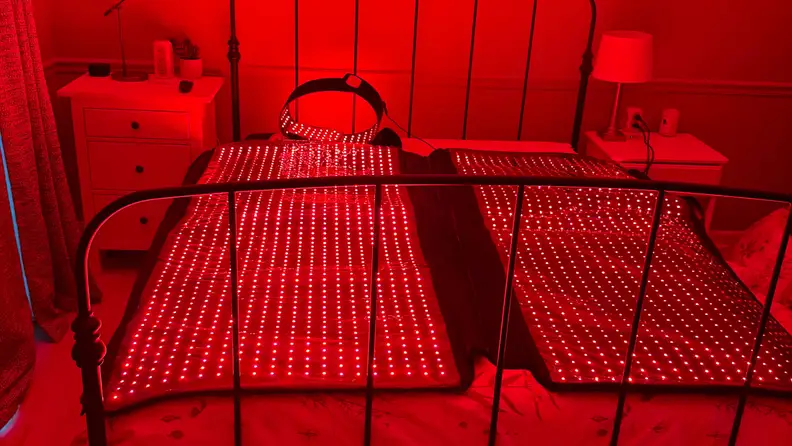 Megelin laser & LED light therapy bag turned on and open on a bed, glowing with red LED light.