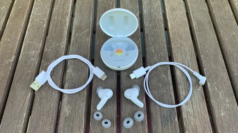 The LG T90Q earbuds with two extra sets of ear tips, two USB-C cables, and their open case all sitting on a wooden table outdoors.