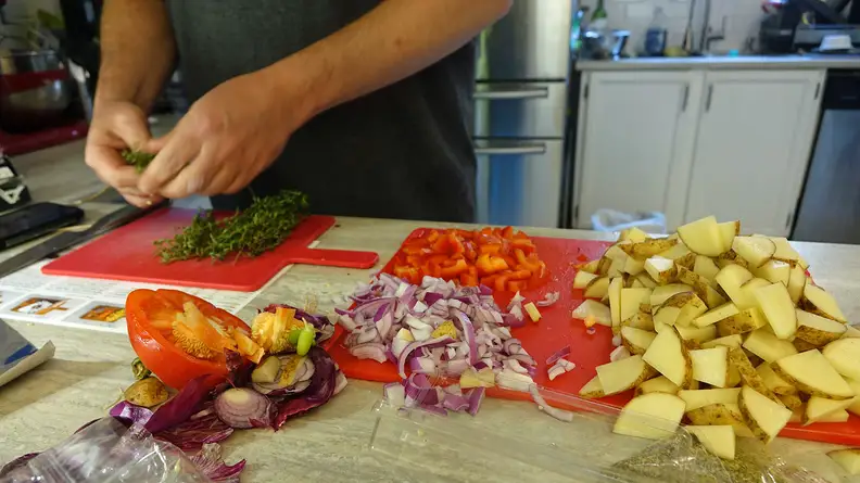 A person prepping herbs and vegetables on a kitchen counter.