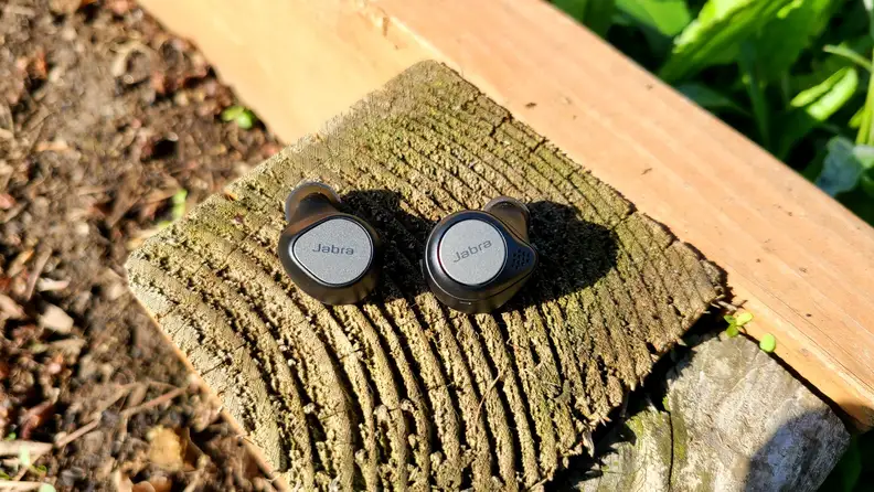The black and silver Elite 7 Pro (left) sit next to the similarly designed Elite Active 75t (right) on a cedar bench.