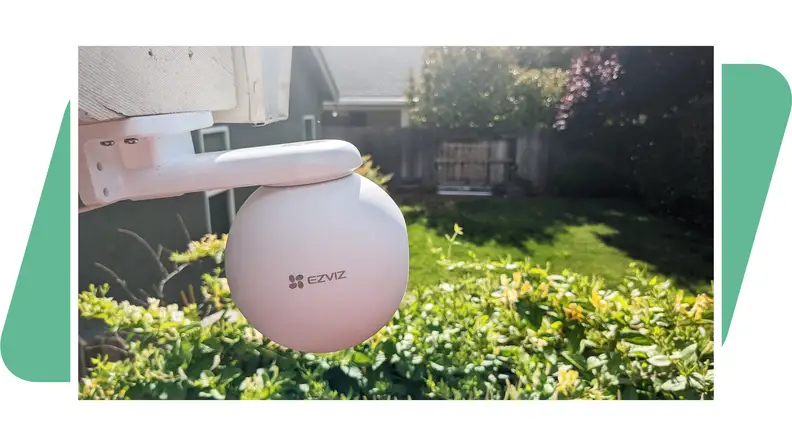 The  EzViz H8 Pro 3K outdoor camera, mounted to a house, facing a backyard with a green background.