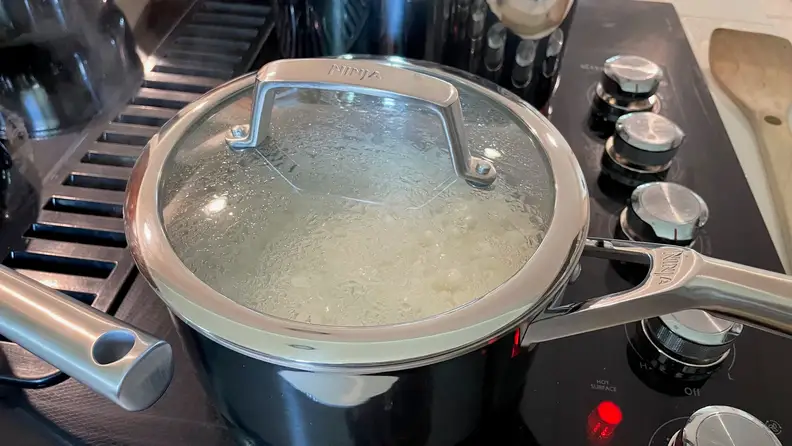 Rice being cooked inside a stainless steel pot, that's on top of a black stove top.